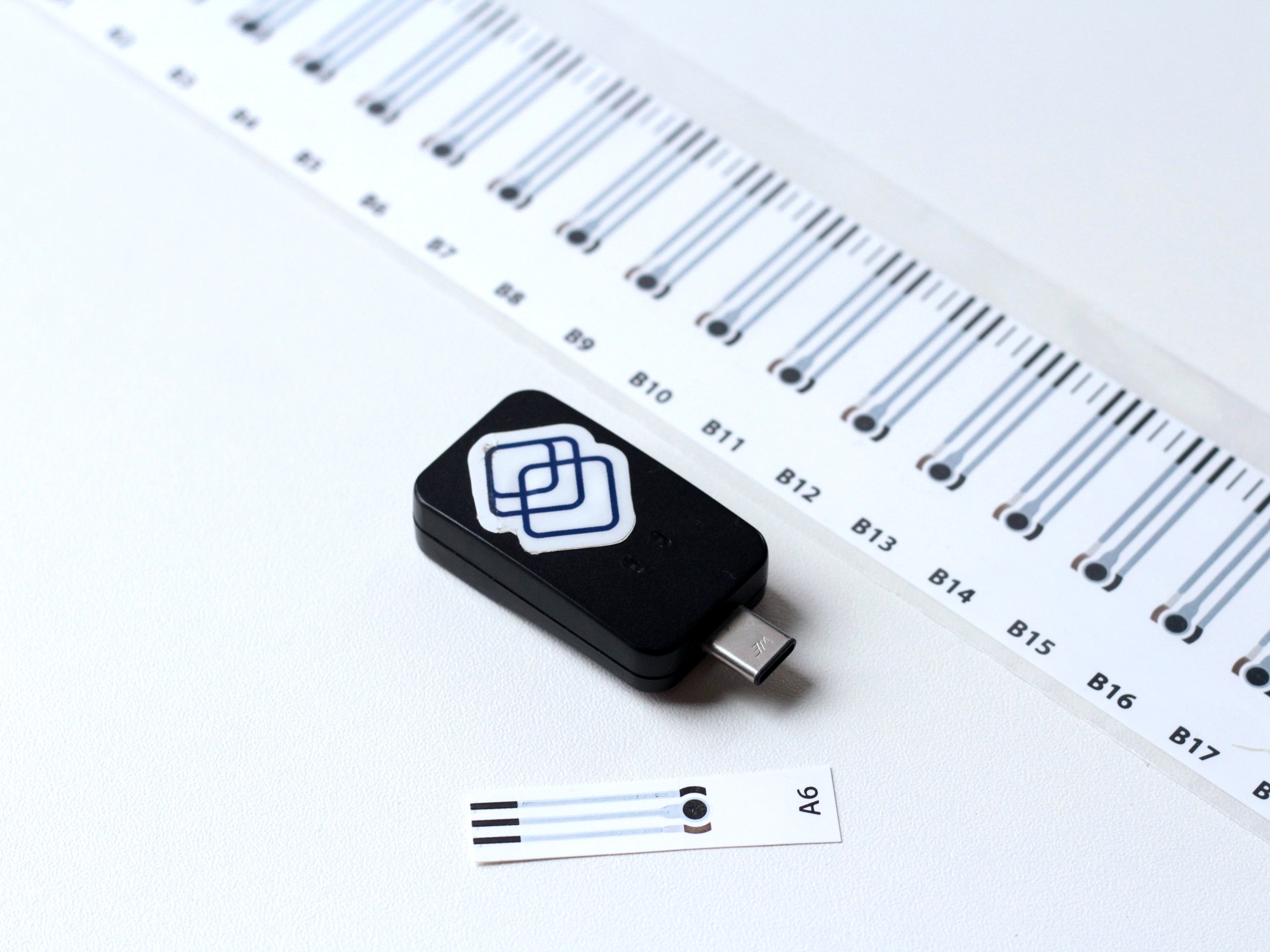 Segura reader alongside a single sensor strip and a full roll of barcoded strips