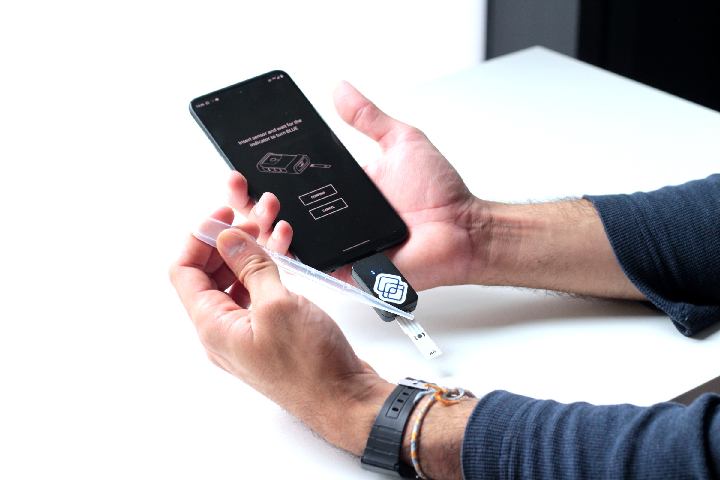 Hands inserting a Segura sensor strip into the reader, with the mobile app visible